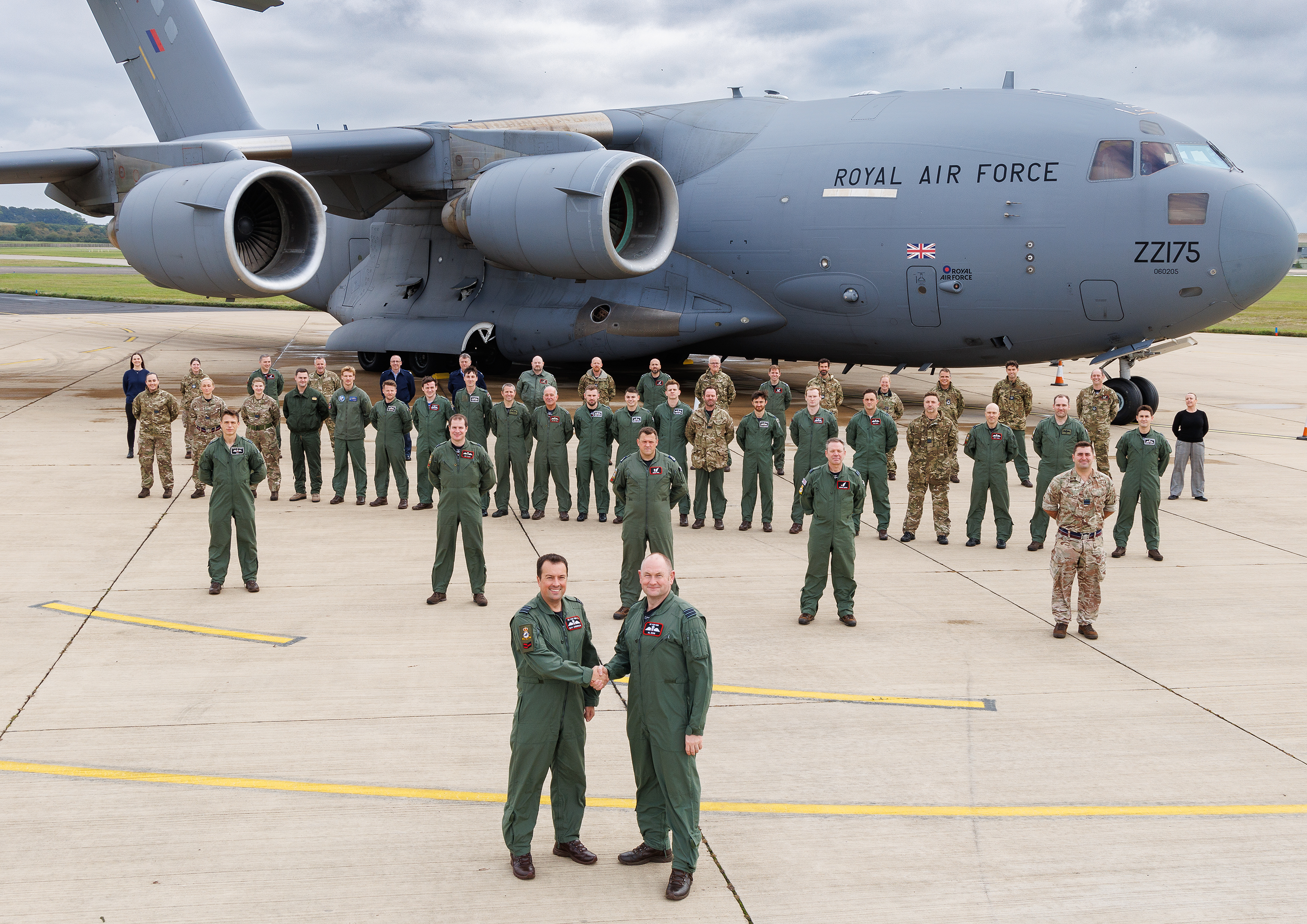 Photo: Wing Commander Gav Anderson (left) and Wing Commander Al Dow (right) shake hands to complete the Squadron Officer Commanding handover, while standing in front of Squadron personnel and a C-17 Globemaster aircraft.